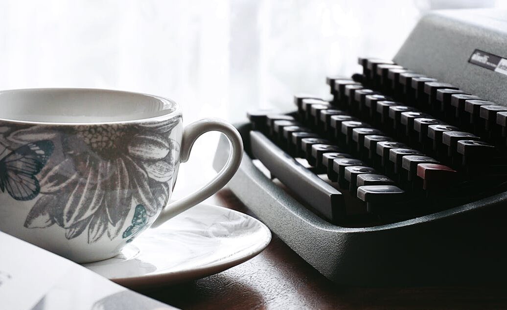 White and Gray Floral Ceramic Cup and Saucer Near Black Typewriter and Book